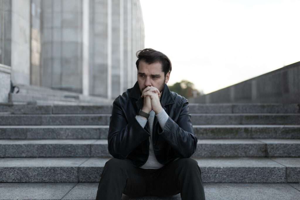 saddened and men sits in depression on the steps of a gray building